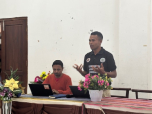Two Asian men sitting at a brown table with a red top speaking.