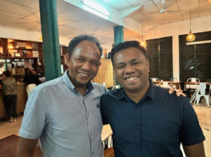 Two Asian men wearing a gray shirt and a black shirt smiling and posing for a photo.