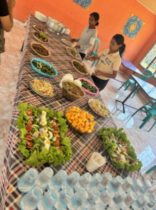 Table with many food dishes in a room with bright orange walls. There are two Asian women with white shirts setting out food. 